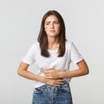 Mulher branca com expressão de desconforto, segurando a mão sobre a região abdominal, indicando síndrome nefrótica